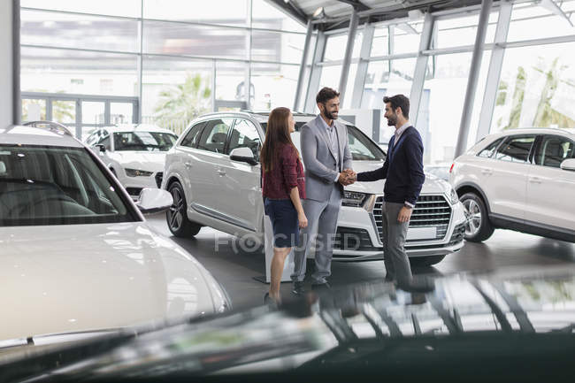 Car salesman and customers handshaking in car dealership showroom — Stock Photo