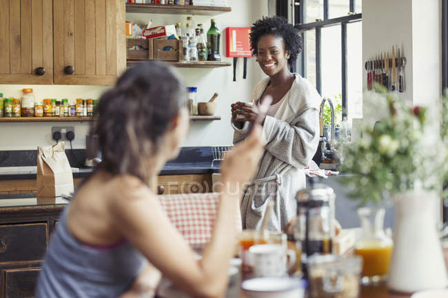 Улыбающаяся лесбийская пара наслаждается кофе и завтраком на кухне — стоковое фото