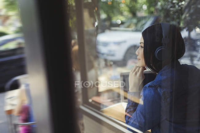 Jeune femme pensive écoutant de la musique avec des écouteurs regardant loin de la fenêtre du café — Photo de stock