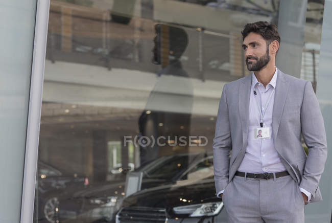 Retrato confiado vendedor de coches mirando hacia otro lado fuera concesionario de coches sala de exposición - foto de stock
