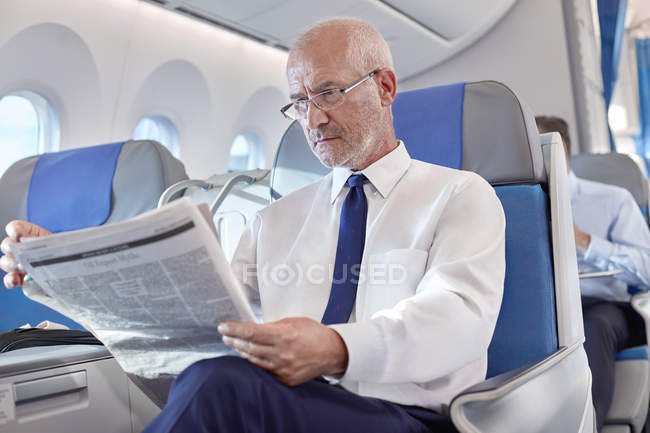 Empresário sênior lendo jornal no avião — Fotografia de Stock