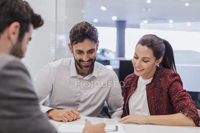 Car salesman explaining financial contract paperwork to couple customers in car dealership office — Stock Photo