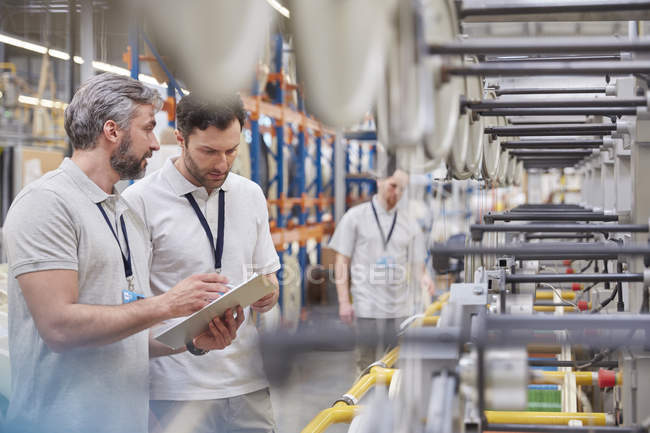Male supervisor and worker with clipboard talking in fiber optics factory — Stock Photo
