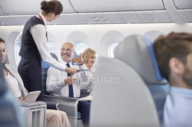 Asistente de vuelo sirviendo whisky a hombre de negocios en primera clase en avión - foto de stock