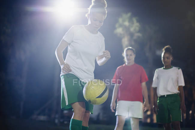 Jovem jogadora de futebol focada praticando em campo à noite, joelhando a bola — Fotografia de Stock