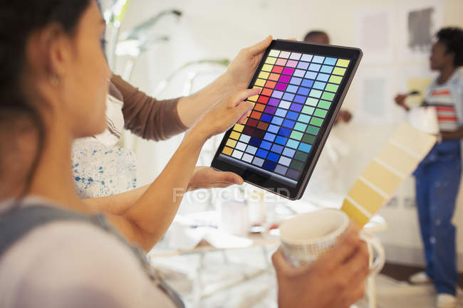 Молодая женщина пьет кофе и смотрит цифровые образцы краски на цифровой планшет — стоковое фото
