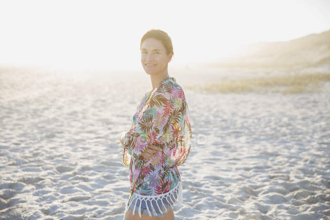 Портрет усміхнений, впевнена брюнетка в купальнику на сонячному літньому пляжі заходу сонця — стокове фото