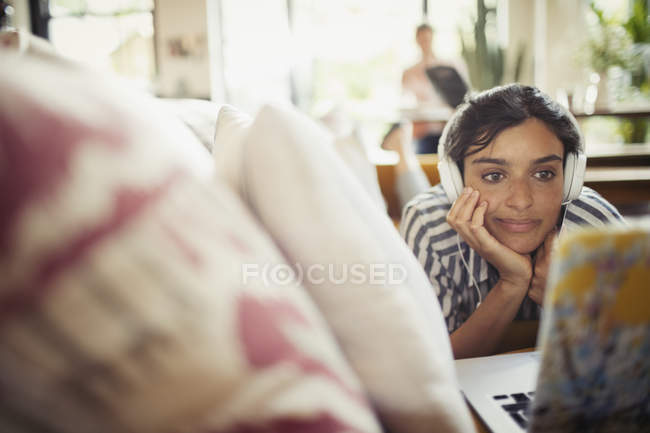 Junge Frau mit Kopfhörer mit Laptop auf Wohnzimmersofa — Stockfoto
