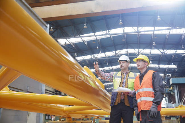 Male foreman with clipboard explaining to worker in factory — Stock Photo