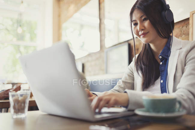 Молода жінка використовує ноутбук і п'є каву в кафе — стокове фото