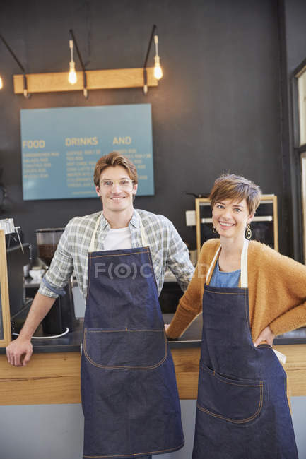 Retrato sonrientes propietarios de café con delantales de mezclilla en la cafetería - foto de stock