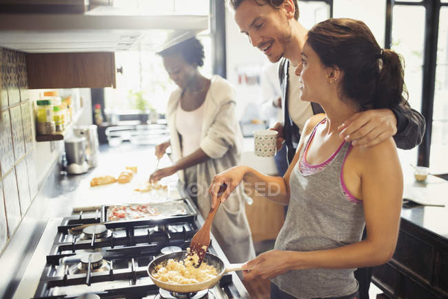 Young couple cooking scrambled eggs on stove in kitchen — Stock Photo
