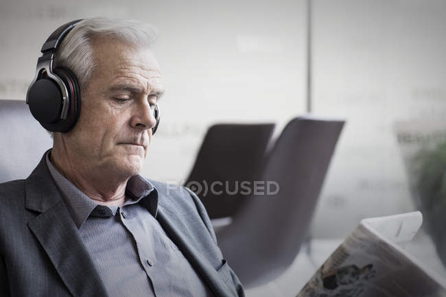 Senior-Geschäftsmann mit Kopfhörern hört Musik und liest Zeitung — Stockfoto