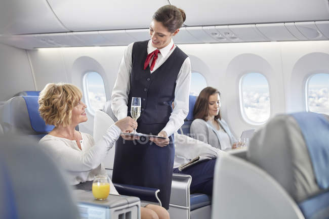 Auxiliar de vuelo sirviendo champán a mujer en primera clase en avión - foto de stock