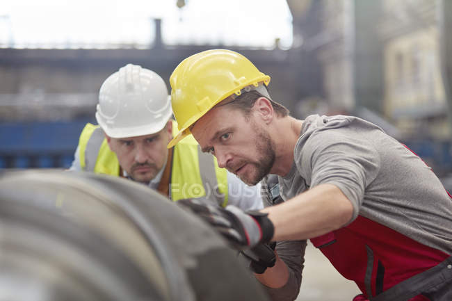 Орієнтовані чоловіки-інженери вивчають сталеву частину на заводі — стокове фото