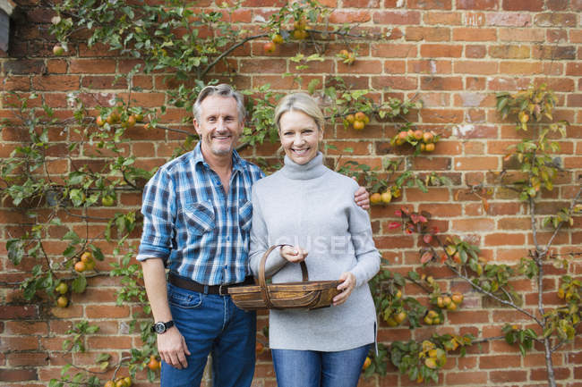 Mature caucasian couple standing with fruit basket at garden — Stock Photo