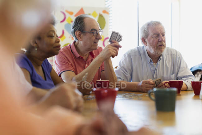Amigos mayores jugando a las cartas en la mesa del centro comunitario - foto de stock