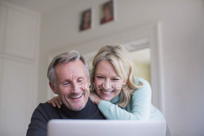 Посміхаючись, щаслива зріла пара використовує ноутбук — стокове фото