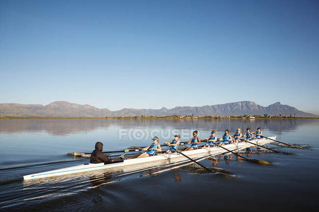 Rameurs femelles ramant sur un lac ensoleillé sous le ciel bleu — Photo de stock