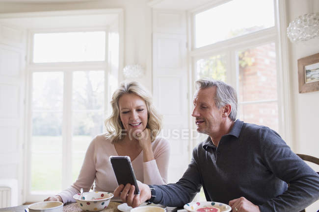 Couple d'âge mûr utilisant un téléphone intelligent à la table du petit déjeuner — Photo de stock