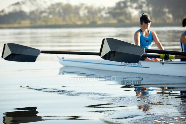 Female rower with oar rowing scull on lake — Stock Photo