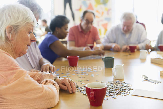 Seniorin setzt Puzzle mit Freunden am Tisch im Gemeindezentrum zusammen — Stockfoto