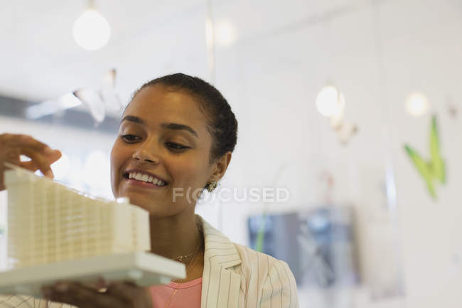 Sonriente, confiada arquitecta examinando modelo en la oficina - foto de stock