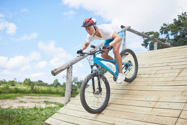 Focused mature man mountain biking down obstacle course ramp — Stock Photo