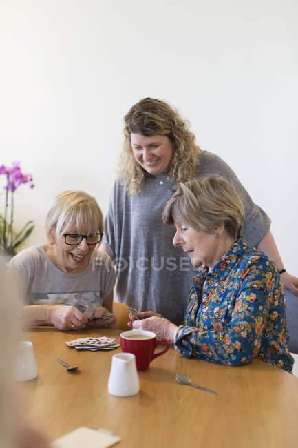 Волонтер дивиться, як старші жінки грають карти за столом у громадському центрі — стокове фото