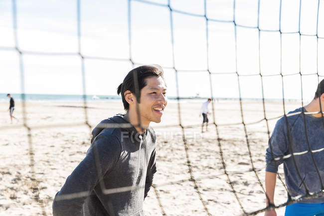 Uomo sorridente che gioca a beach volley sulla spiaggia soleggiata — Foto stock