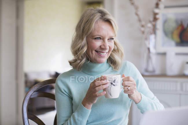 Усміхнена зріла жінка п'є каву в сучасному будинку — стокове фото