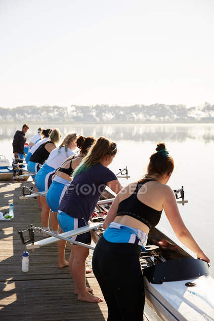 Female rowers lowering scull from lakeside dock — Stock Photo