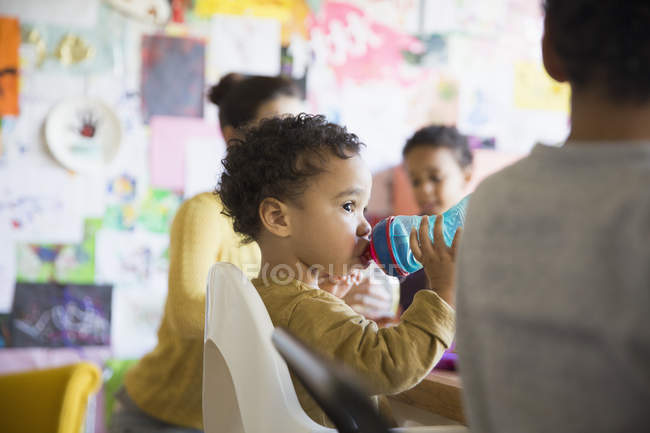 Mother with african american sons at kitchen, boy drinking from baby bottle — Stock Photo