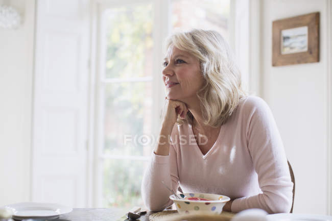 Sorrindo, satisfeita mulher madura tomando café da manhã — Fotografia de Stock