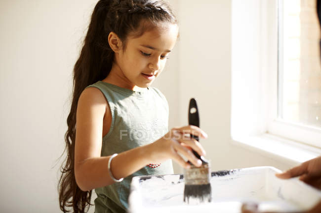 Girl painting, dipping paintbrush in tray — Stock Photo