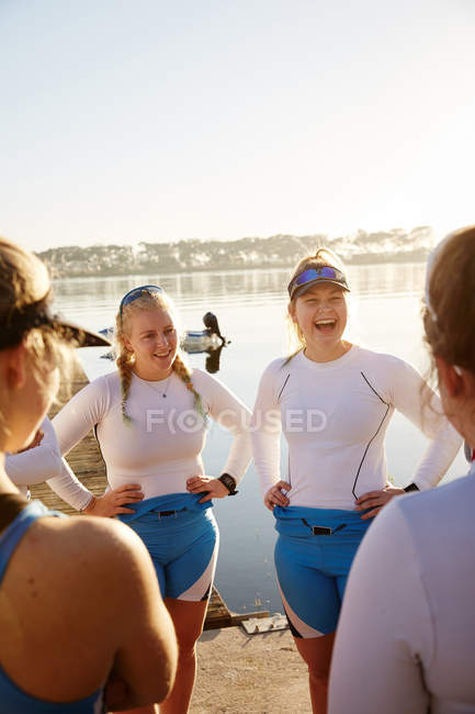 Equipe de remo feminino rindo e falando ao lado do lago ensolarado — Fotografia de Stock