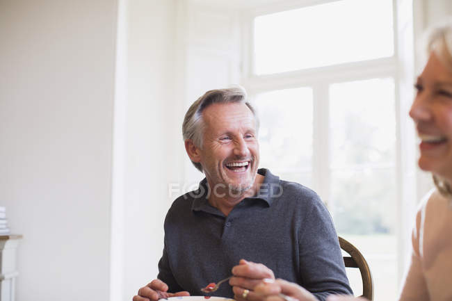 Riendo pareja madura comiendo en casa moderna - foto de stock
