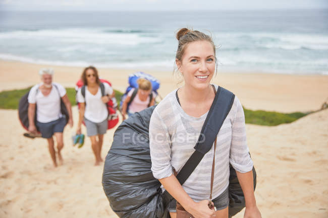 Retrato sonriente, confiado parapente femenino llevando mochila paracaídas en la playa - foto de stock