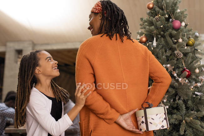 Madre escondiendo regalo de Navidad de hija curiosa - foto de stock