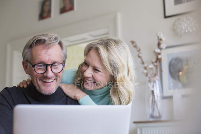 Sorridente coppia matura utilizzando il computer portatile a casa moderna — Foto stock