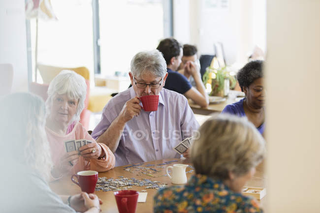 Amigos mayores jugando y tomando té en la mesa en el centro comunitario - foto de stock