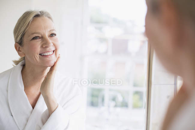 Sorrindo mulher madura tocando rosto no espelho do banheiro — Fotografia de Stock