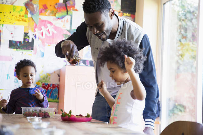 Padre vertiendo jarabe y gofres para la hija del niño emocionado - foto de stock