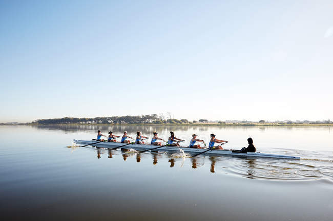 Female rowing team rowing scull on tranquil lake — Stock Photo