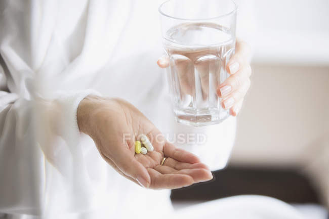 Cropped image of woman taking vitamins with glass of water — Stock Photo
