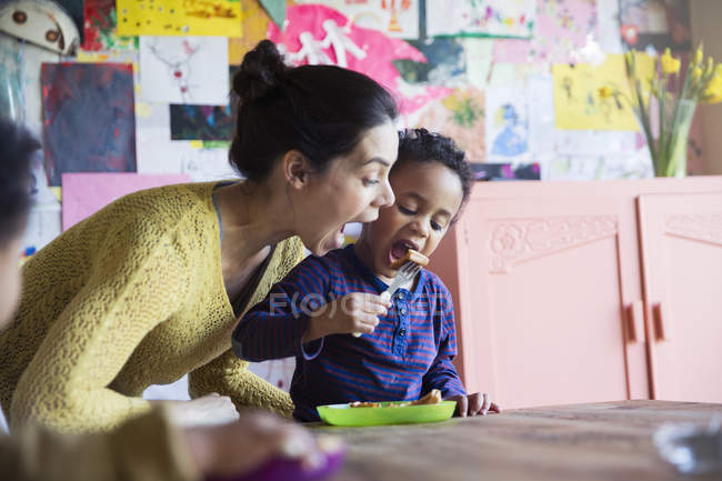 Glückliche kaukasische Mutter mit afrikanisch-amerikanischem Sohn beim Essen in der Küche — Stockfoto