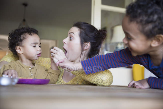 Madre caucásica feliz alimentación hijo en la cocina, familia multirracial - foto de stock