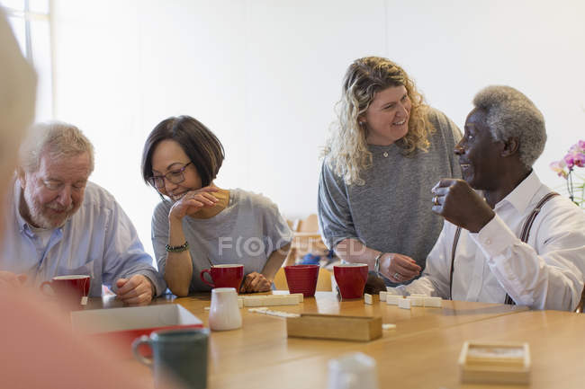 Voluntario hablando con el hombre mayor jugando juegos en la mesa en el centro comunitario - foto de stock