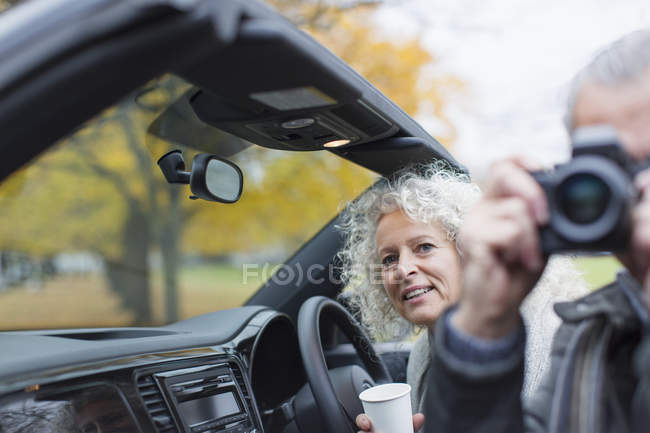 Senior couple using digital camera in convertible — Stock Photo