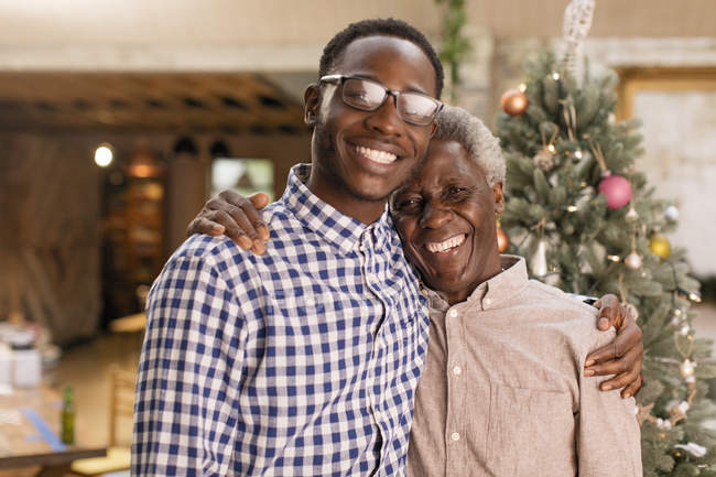 Портрет улыбающийся дедушка и внук обнимаются перед елкой — стоковое фото